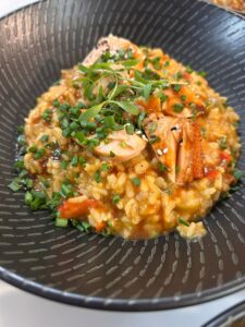 Risotto cremoso con salmón y cebollino en plato negro, cocina casera de La Mesa